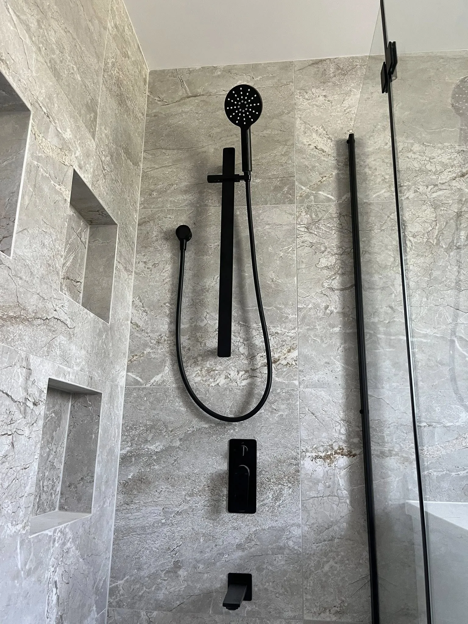 Rainfall shower installation with matte black tapware and recessed shelving